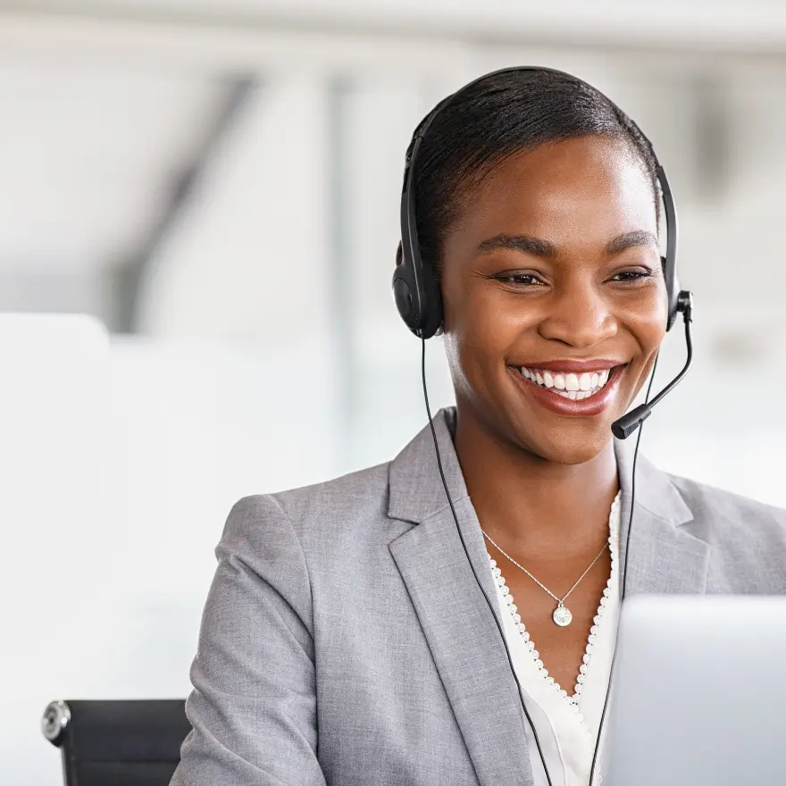 Une Femme souriante portant un casque, utilisant un ordinateur portable avec enthousiasme.