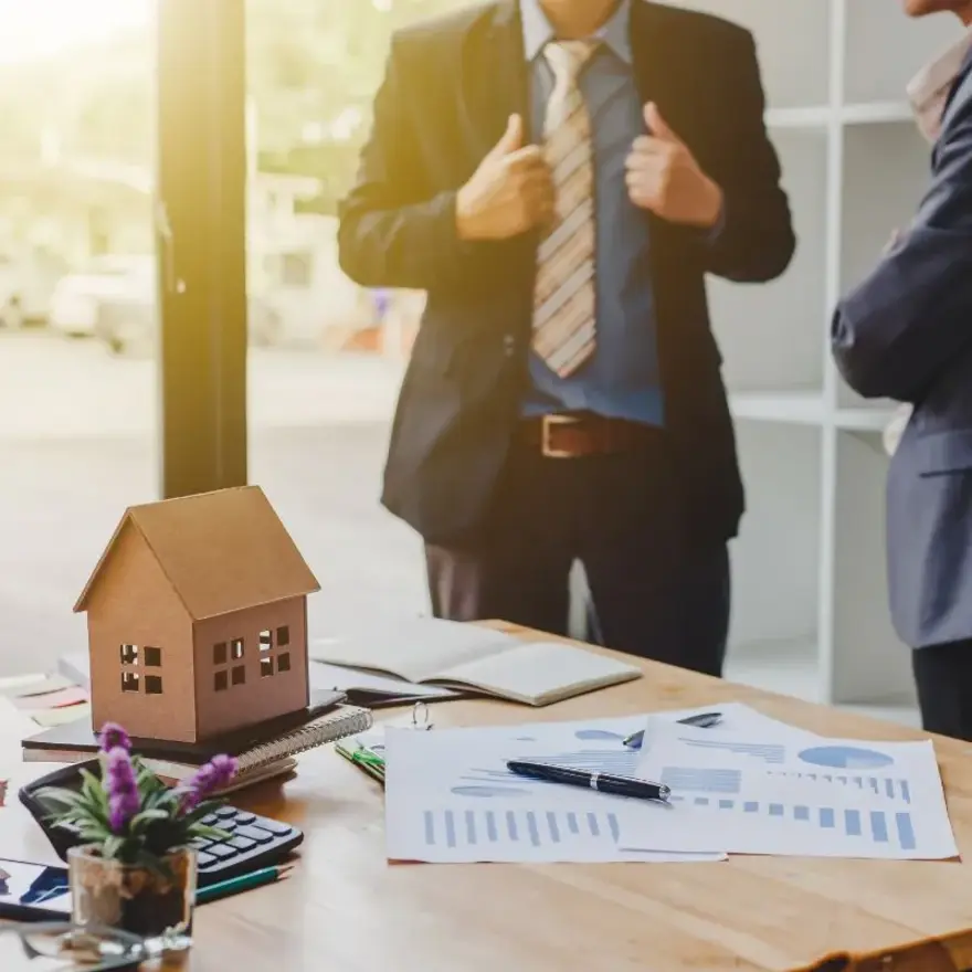 Deux professionnels se tenant devant un modèle de maison, discutant de projets immobiliers.