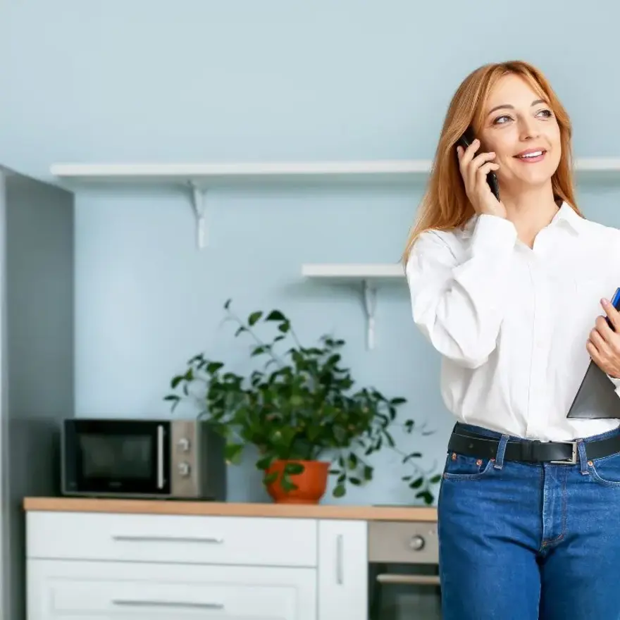 Une femme en chemise blanche et jeans parle au téléphone.