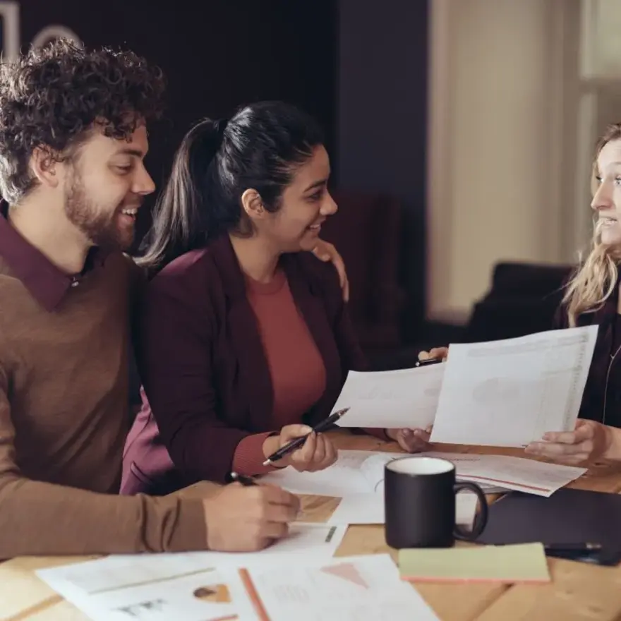 Trois personnes assises à une table, examinant des documents et utilisant un stylo.